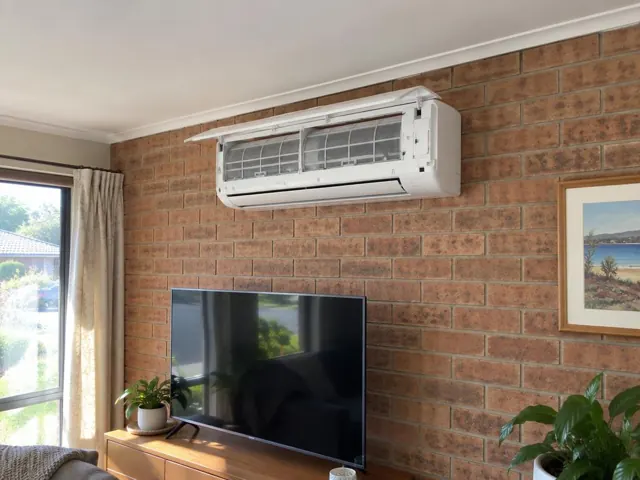 Clean split system with open front panel and visible filters on a brick living room wall in Reynella