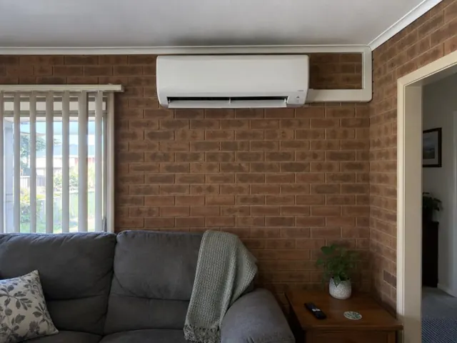 Clean split-system indoor head on a brick feature wall above a sofa in a living room in Happy Valley