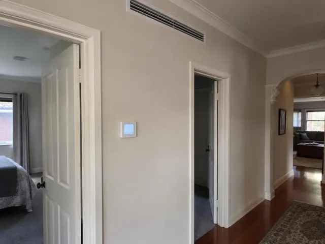Hallway ceiling return-air grille and wall controller in a cream home interior in Morphett Vale